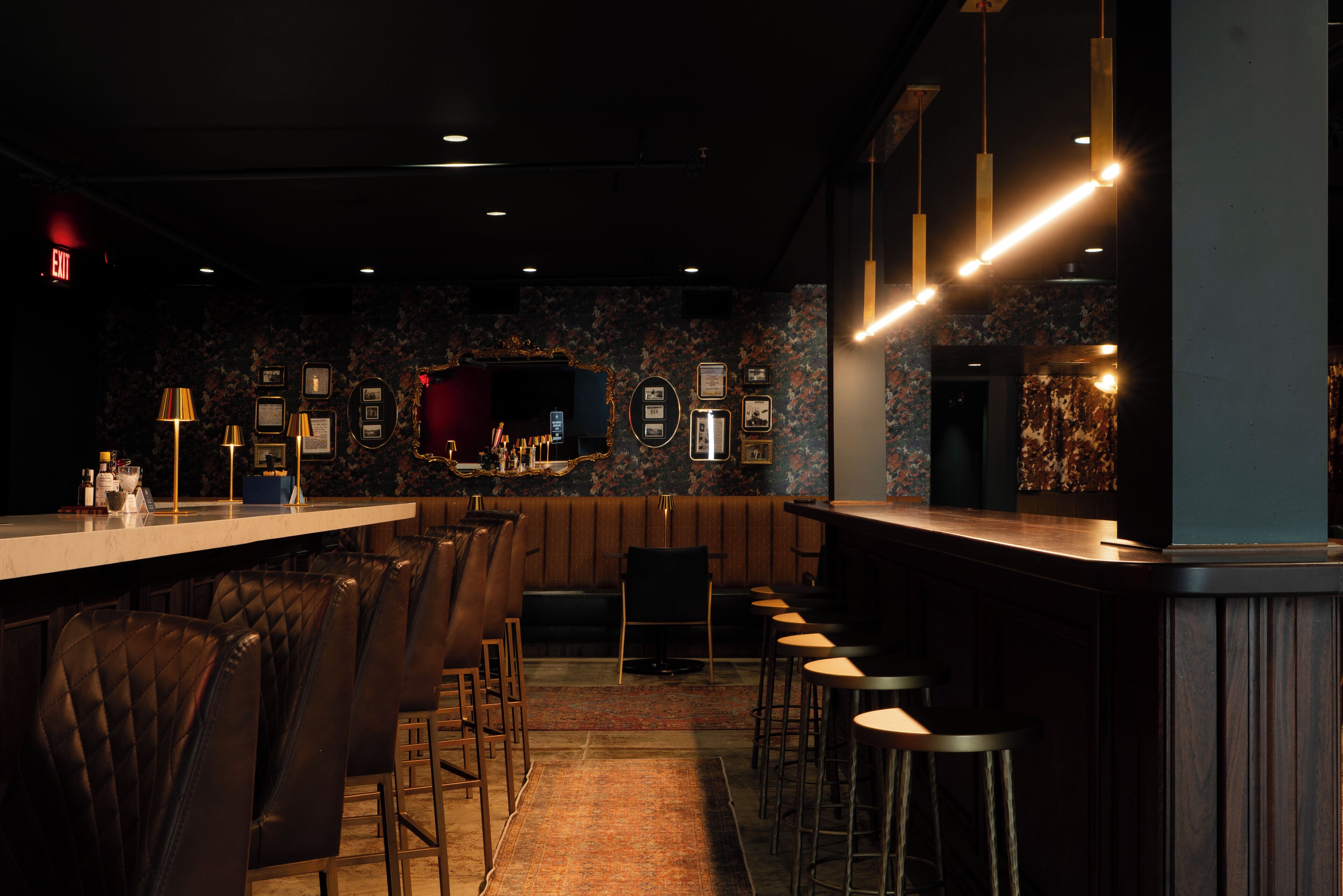 A bar area with a long counter, multiple stools, and framed pictures on the wall.