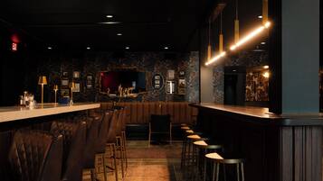 A bar area with a long counter, multiple stools, and framed pictures on the wall.
