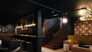 A bar area with a counter, stools, and a staircase leading to a seating area with sofas and a round table. - Hotel Pontotoc  (Memphis)