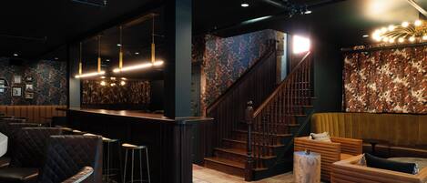 A bar area with a counter, stools, and a staircase leading to a seating area with sofas and a round table.