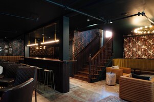 A bar area with a counter, stools, and a staircase leading to a seating area with sofas and a round table.