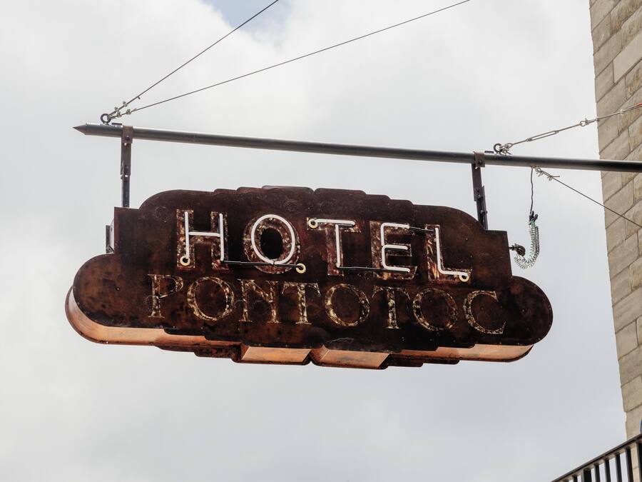 A rustic, weathered sign for a hotel named "HOTEL PONTIFICIO" suspended above a building.