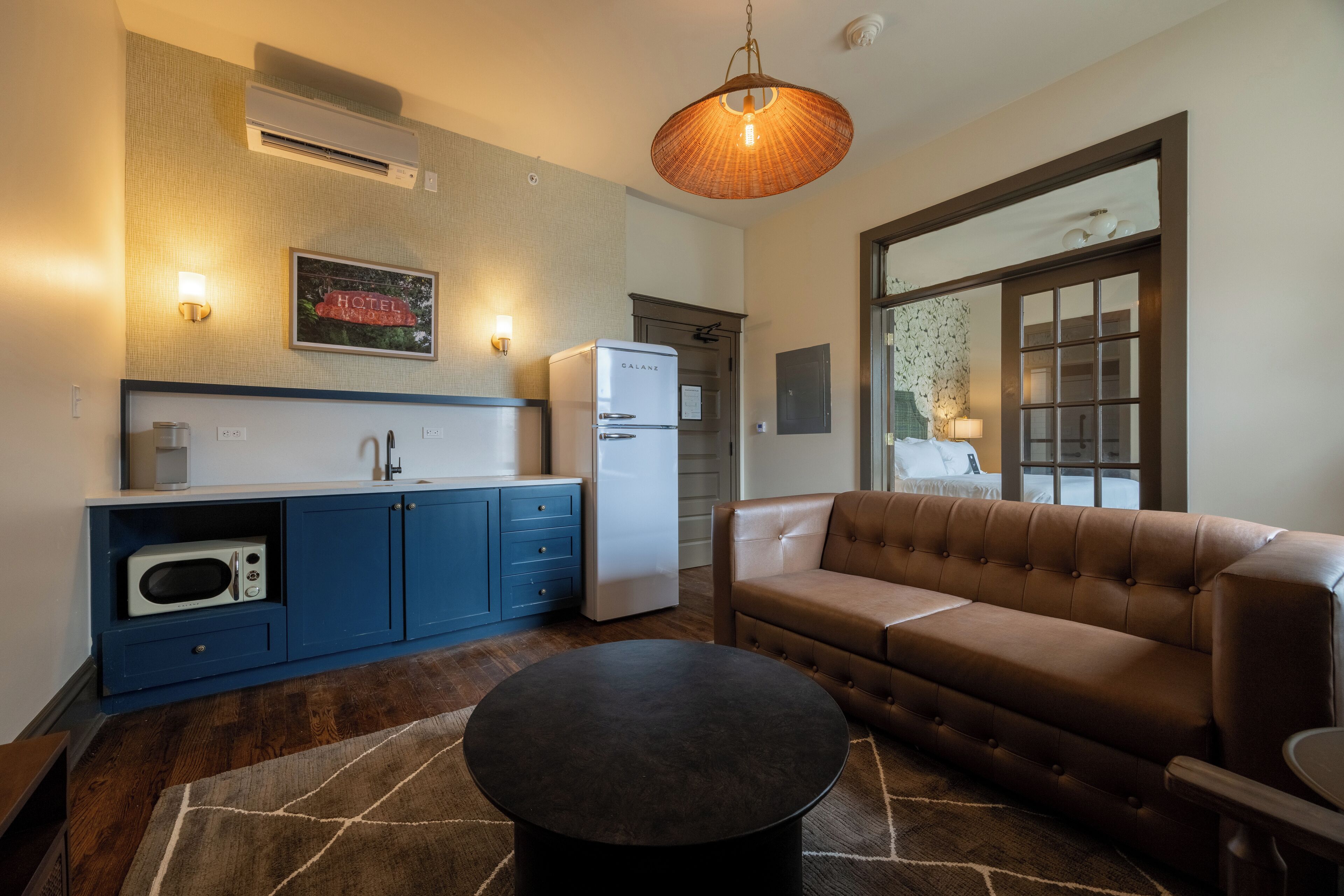 Un espacio habitable compacto con kitchenette, un sofá marrón, una mesita de centro redonda y un amplio ventanal con vistas.