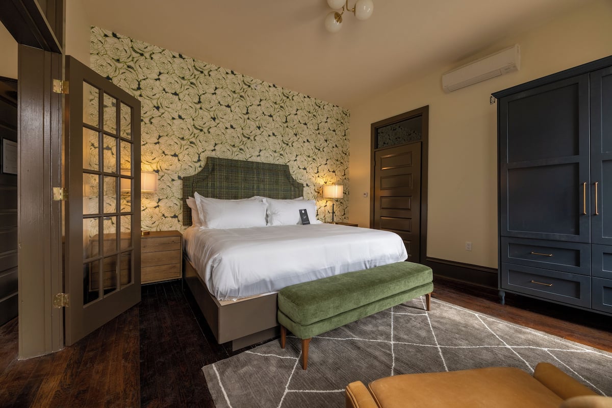 Un dormitorio con una cama grande, un banco verde, una mesita de noche de madera, un armario y una pared con diseño.
