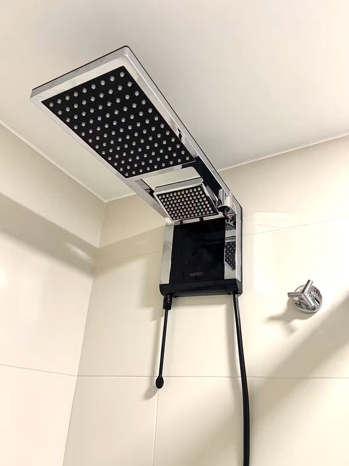 A showerhead with a control panel, mounted on a white tiled wall.