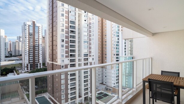 Un balcon avec vue sur des immeubles de grande hauteur, une piscine et une table avec des chaises.