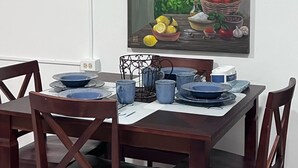 A dining table set with blue plates and cups, a basket of red apples, lemons, and a jar of olives.