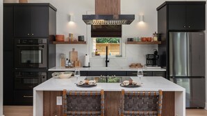 A modern kitchen with black cabinets, a stainless steel refrigerator, and a central island with seating.