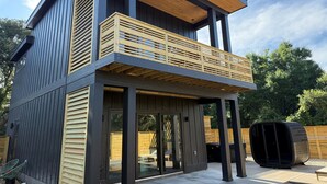A modern two-story house with a balcony, large windows, and a wooden deck.