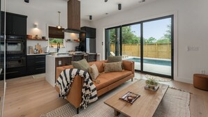 A modern kitchen with dark cabinetry, a central island, and a dining area with a wooden table and sofa.