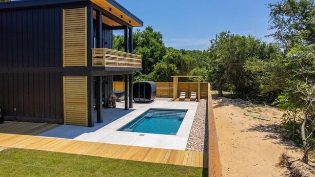 A modern two-story house with a pool, wooden deck, and a fenced backyard.