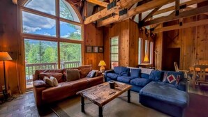 A cozy cabin interior with a large window, wooden walls, a brown leather sofa, a blue sofa, and a wooden coffee table. - Lodge Off Main, Walk to Gondola! (Breckenridge)