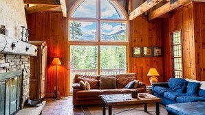 A cozy cabin interior with a stone fireplace, wooden walls, a large arched window, and a wooden ceiling. - Lodge Off Main, Walk to Gondola! (Breckenridge)