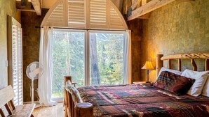 A bedroom with a large window, a bed with patterned bedding, a bedside table with a lamp, and a wooden bench. - Lodge Off Main, Walk to Gondola! (Breckenridge)