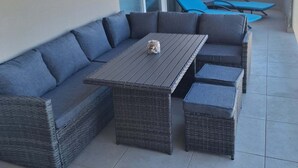 Ein Balkon mit einer grauen Eckcouch, einem Holztisch und blauen Lounge-Stühlen.