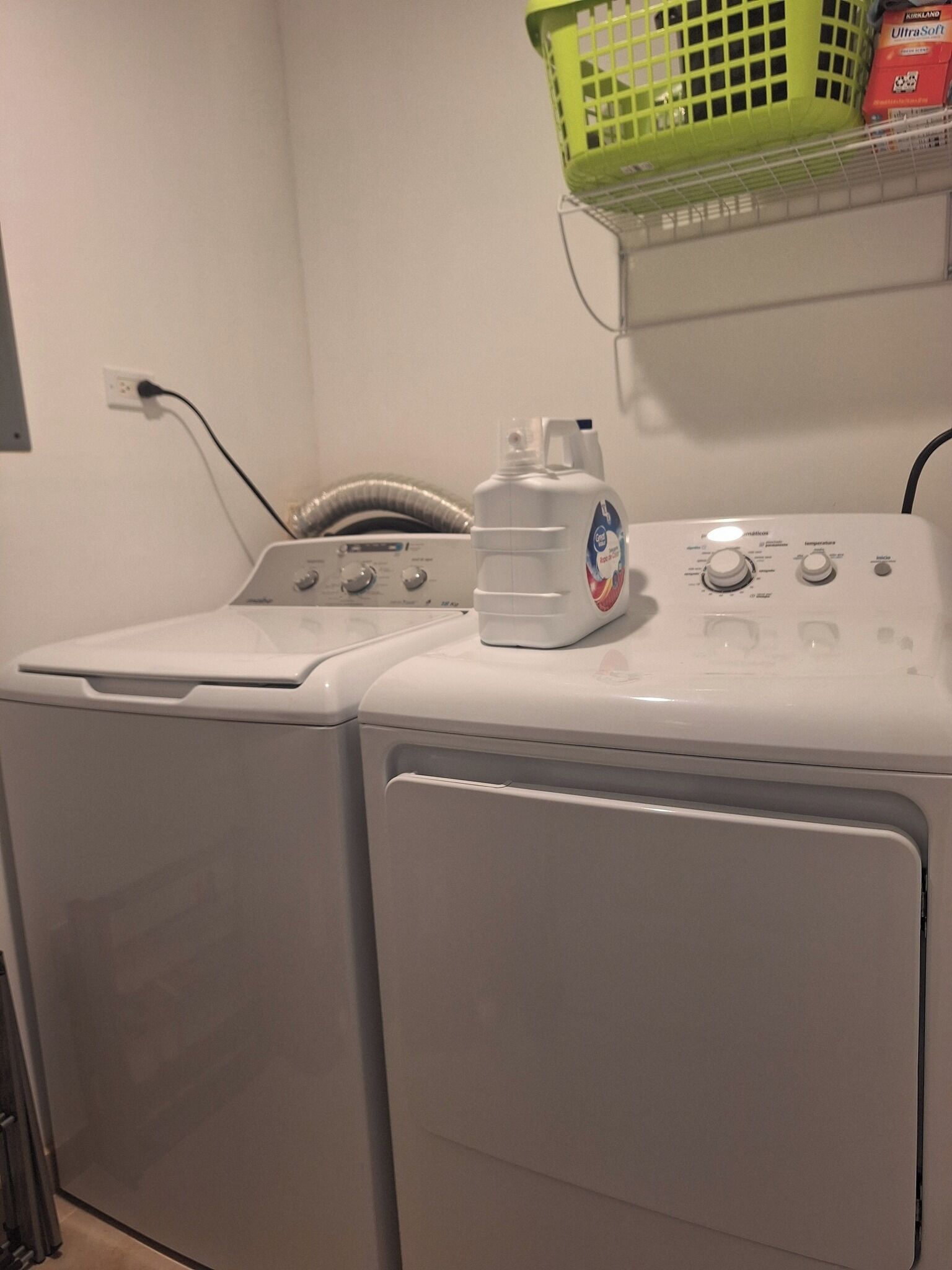 Un lave-linge et un sèche-linge à chargement frontal, dotés d’un panneau de commande, un panier à linge vert et une bouteille de lessive placés sur le dessus.