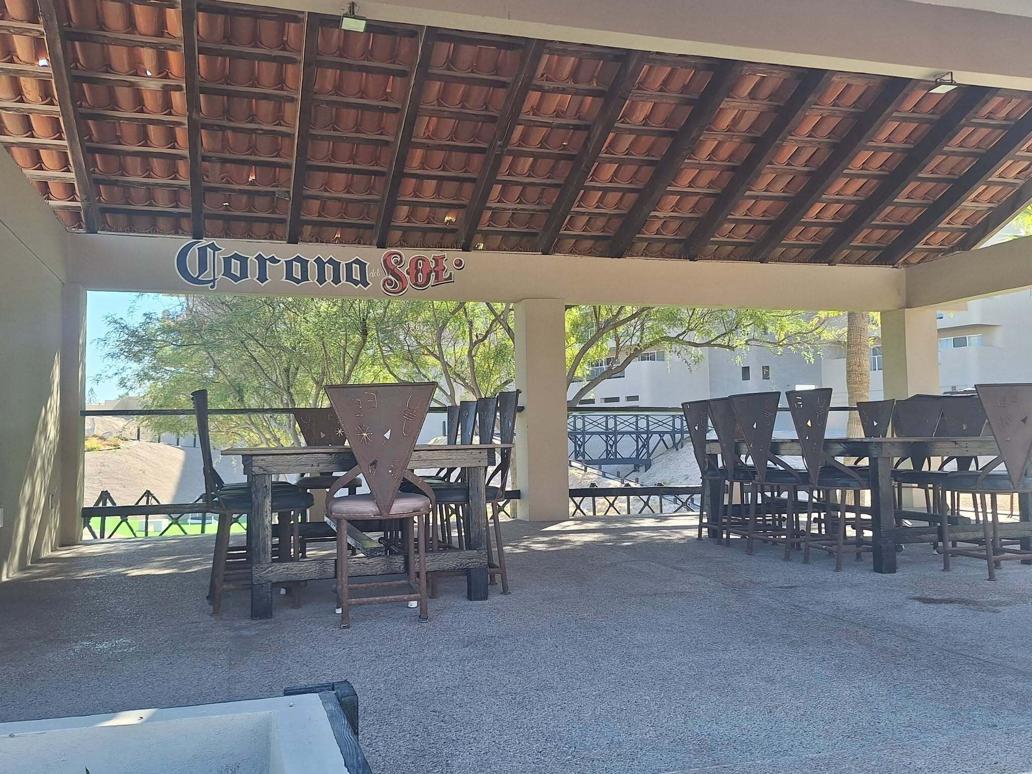 An outdoor patio area with tables and chairs, a sign reading "Corona Sol", and a view of a bridge and buildings in the background.