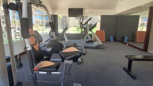 Une salle de sport équipée de matériel d’exercice, d’un téléviseur et dotée de grandes fenêtres.