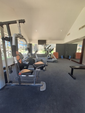 A gym with exercise equipment, a television, and large windows.