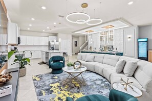 A modern living room with a sectional sofa, a coffee table, and a dining area with a kitchen in the background.