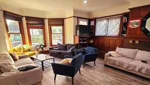 A cozy living room with a sofa, armchairs, and a coffee table. There are wooden floors and a window with blinds.