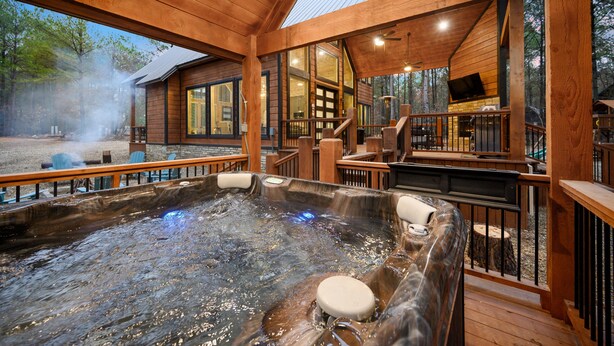 A hot tub area with wooden deck, large windows, and a fireplace.