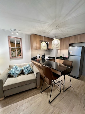 A modern kitchen with wooden cabinets, a dining table with chairs, a built-in oven, and a refrigerator.