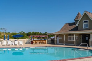 A swimming pool with lounge chairs and umbrellas, a bar area, and a covered seating area.