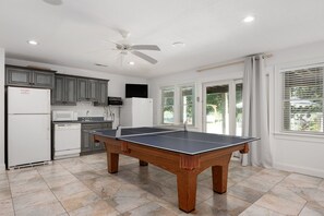 Eine geräumige Küche mit Tischtennisplatte, Kühlschrank, Mikrowelle und Deckenventilator.