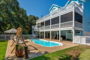 A two-story house with a swimming pool, outdoor seating, and a covered patio area.