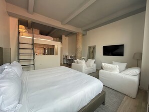 A modern hotel room with a large bed, two white sofas, a small table, and a TV on the wall. - Designer Luxe Loft, with Housekeeping & Doorman - Greenwich Village/Noho (New York)