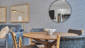 Un coin repas avec une table ronde, des chaises, un bol, un miroir et un mur décoré de motifs.