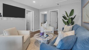 Un salon moderne avec un canapé bleu, des fauteuils blancs, une table basse en marbre et un ventilateur de plafond.