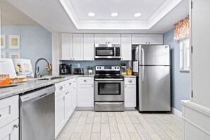 A modern kitchen with white cabinets, stainless steel appliances, a built-in oven, and a refrigerator.