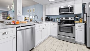 A modern kitchen with white cabinets, stainless steel appliances, and a wooden floor. - Cocoa Beach Oceanfront | Sunrise Views, Heated Pool & BBQ Grill | Walk to Downtown (Cocoa Beach)