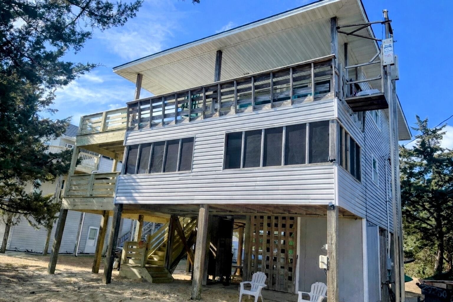 A two-story building with a balcony on the upper floor, a staircase leading to the upper level, and a covered outdoor area with chairs.