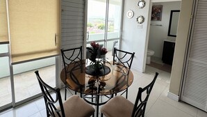 Un coin repas comprenant une table ronde en verre, quatre chaises et une fenêtre avec des stores.