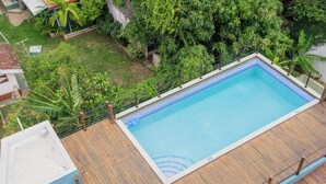 Une piscine rectangulaire entourée d’une terrasse en bois, le tout se fondant dans un décor de verdure luxuriante.