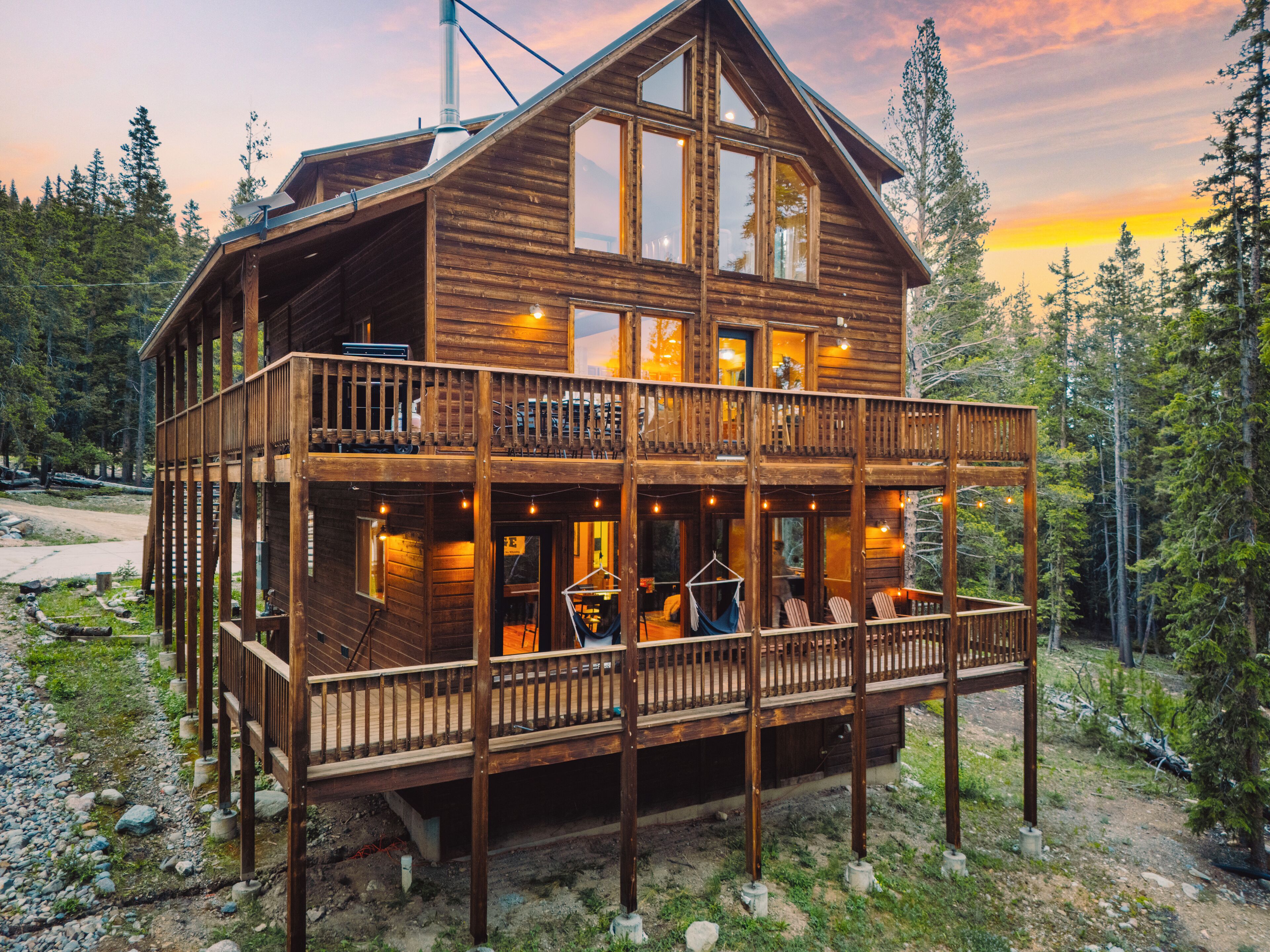 A two-story wooden cabin with a balcony, surrounded by trees.