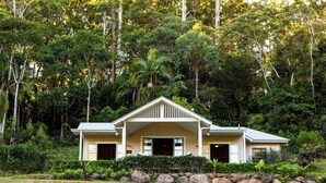 A two-story house with a gabled roof, surrounded by dense forest. - Rainforest Retreat | Fire, Stars & Birdsong | Byron Bay Hinterland (Dorroughby)
