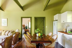 A dining area with a wooden table and wicker chairs, a green door, and white kitchen cabinets.