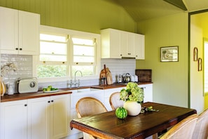A kitchen with white cabinets, a wooden table, wicker chairs, and a window with a view of greenery.