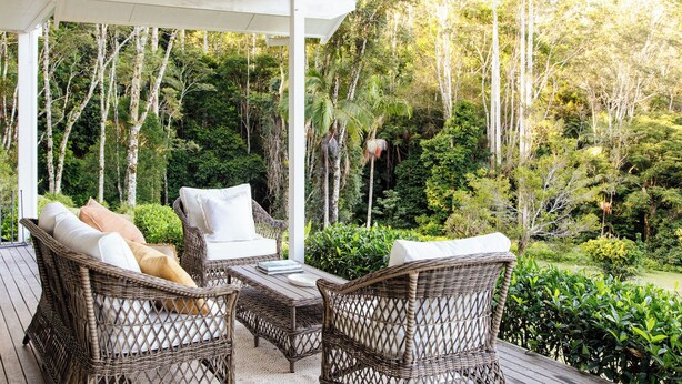 A covered outdoor seating area with wicker furniture and a view of a dense forest. - Rainforest Retreat | Fire, Stars & Birdsong | Byron Bay Hinterland (Dorroughby)