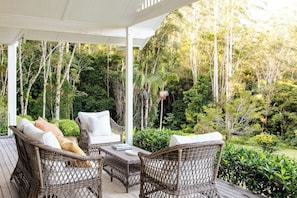 A covered outdoor seating area with wicker furniture and a view of a dense forest.