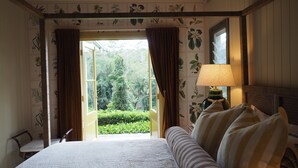 A bedroom with a large bed, a nightstand, a lamp, and a view of greenery through an open window. - Rainforest Retreat | Fire, Stars & Birdsong | Byron Bay Hinterland (Dorroughby)