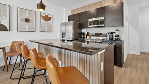 A modern kitchen with a central island, bar stools, a microwave, and a coffee machine. - 3231 ED - The Hub Modern 3BR (Kissimmee)