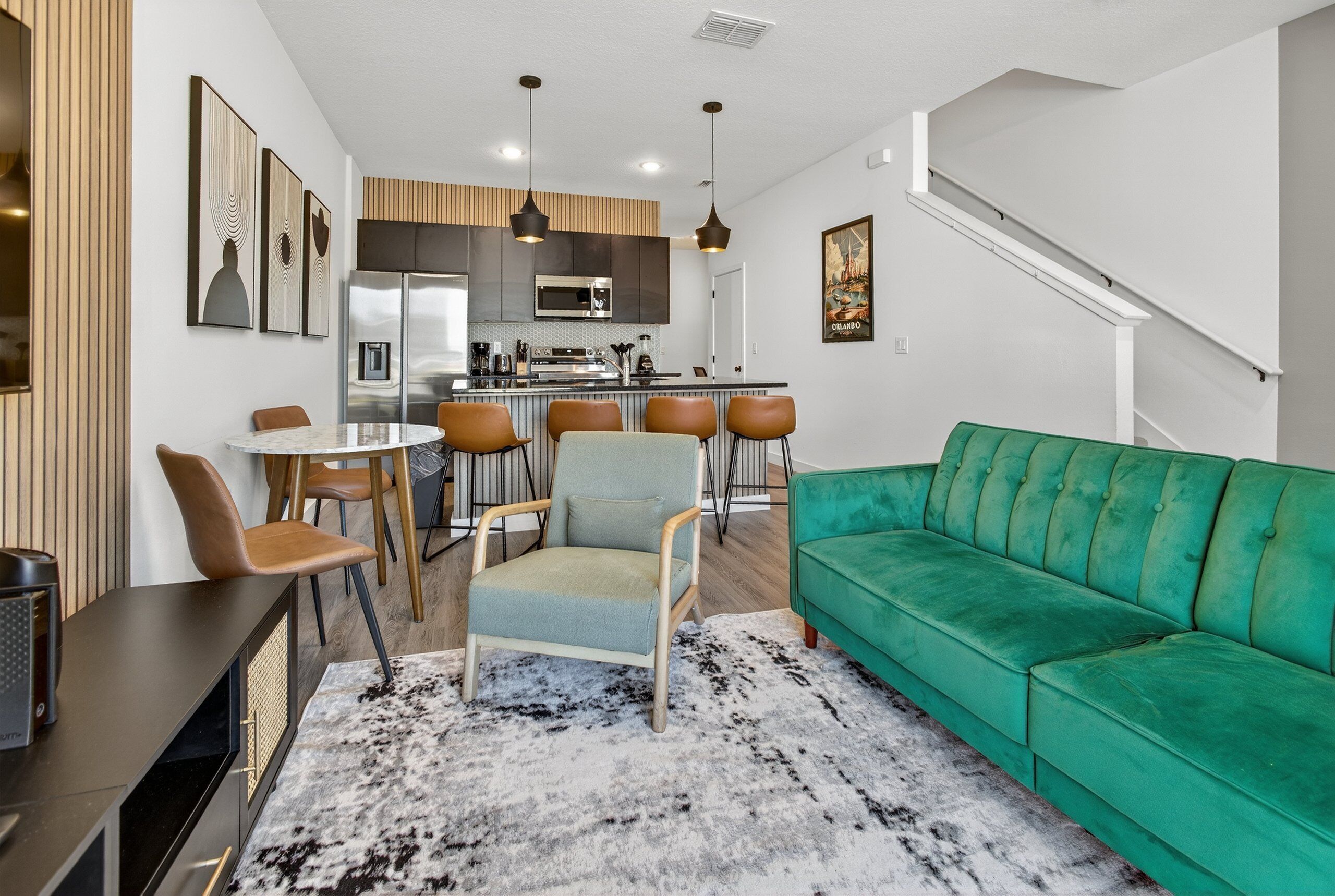 A modern kitchen with a central island, a dining area with a table and chairs, and a green sofa in a living area.