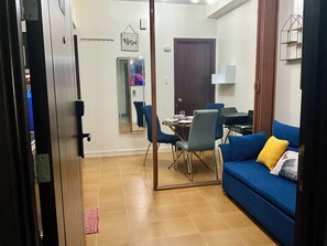 Ein Wohnzimmer mit einem blauen Sofa, einem Esstisch mit Stühlen, einem Spiegel und einer Tür mit dem Schild 'Blessed'.