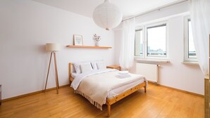 A bedroom with a wooden bed, a bedside lamp, a white radiator, and a window with curtains.