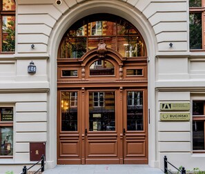 A brown double door with glass panels, a decorative arch above, and a sign indicating the building's name and address.